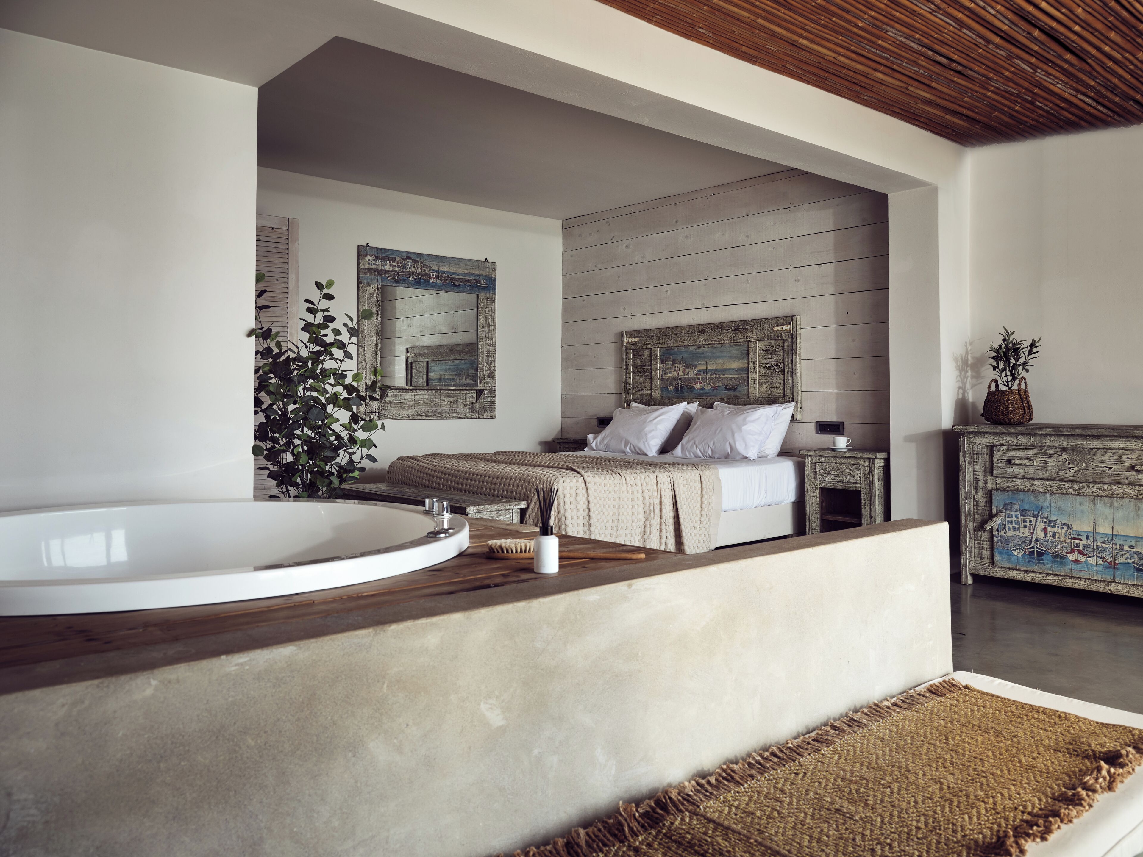 A modern bedroom with a large bathtub, a bed with white linens, and a rustic wooden dresser.