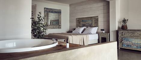 A modern bedroom with a large bathtub, a bed with white linens, and a rustic wooden dresser.
