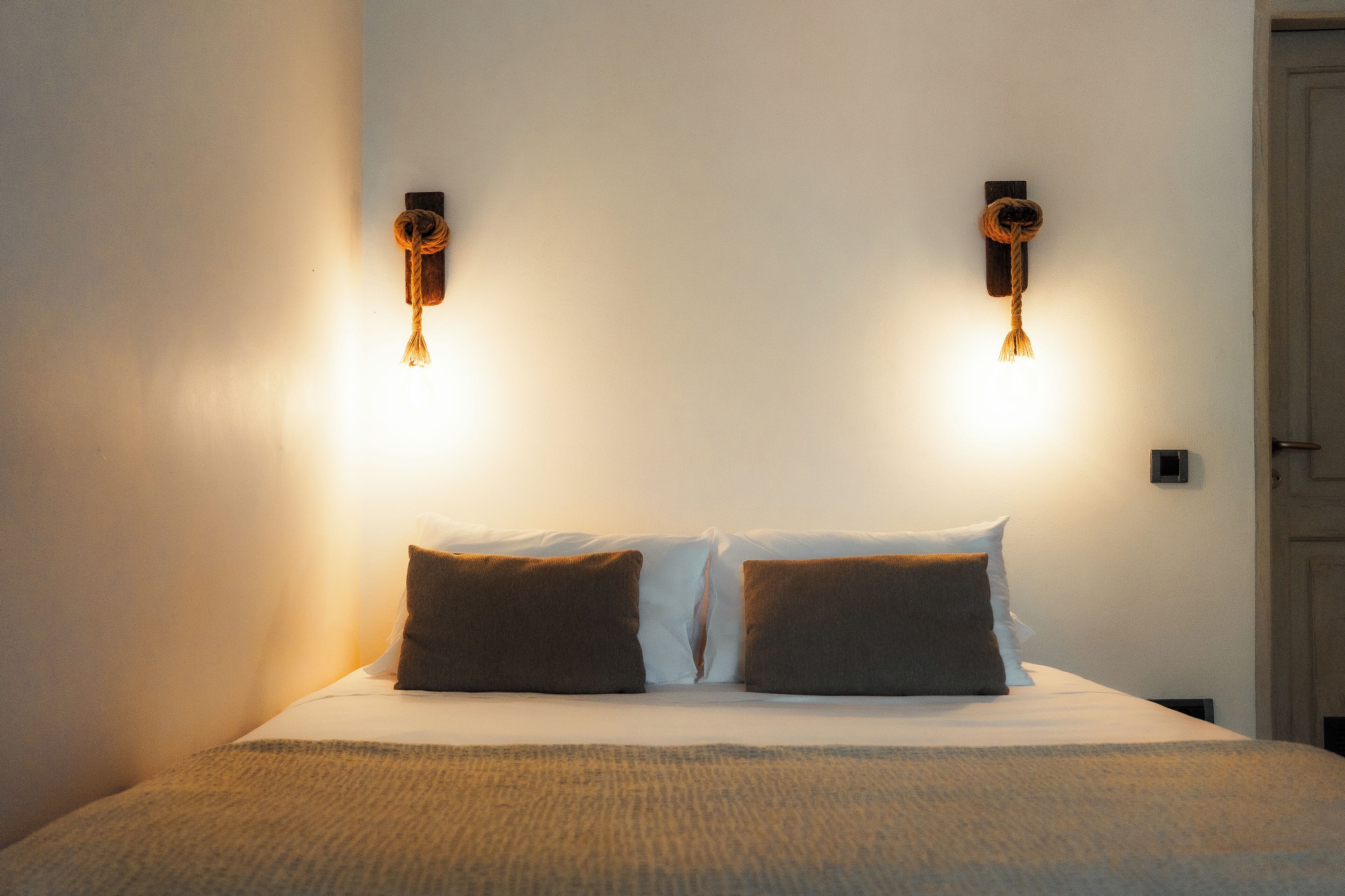 A bed with two pillows and a blanket, a wall-mounted light fixture, and a door.