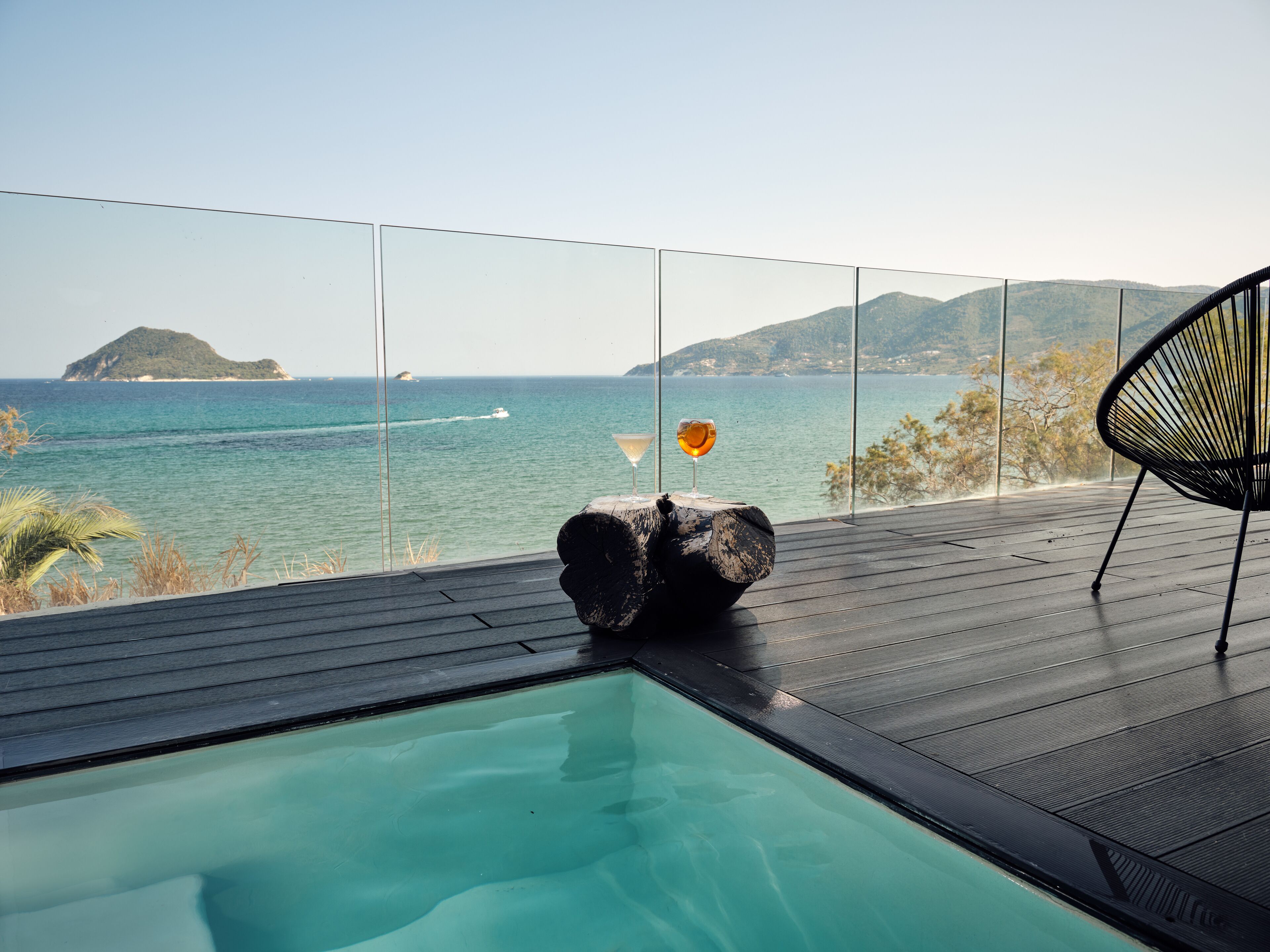 Ein Poolbereich mit Meerblick, ein Stuhl und ein Tisch mit einem Glas.