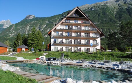 A multi-story hotel with balconies, a swimming pool, and a mountainous backdrop.