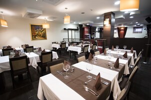 Un restaurante con varias mesas dispuestas para comer, con manteles blancos y servilletas marrones.