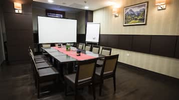 A conference room with a long table, chairs, a projector screen, a whiteboard, and a painting on the wall.