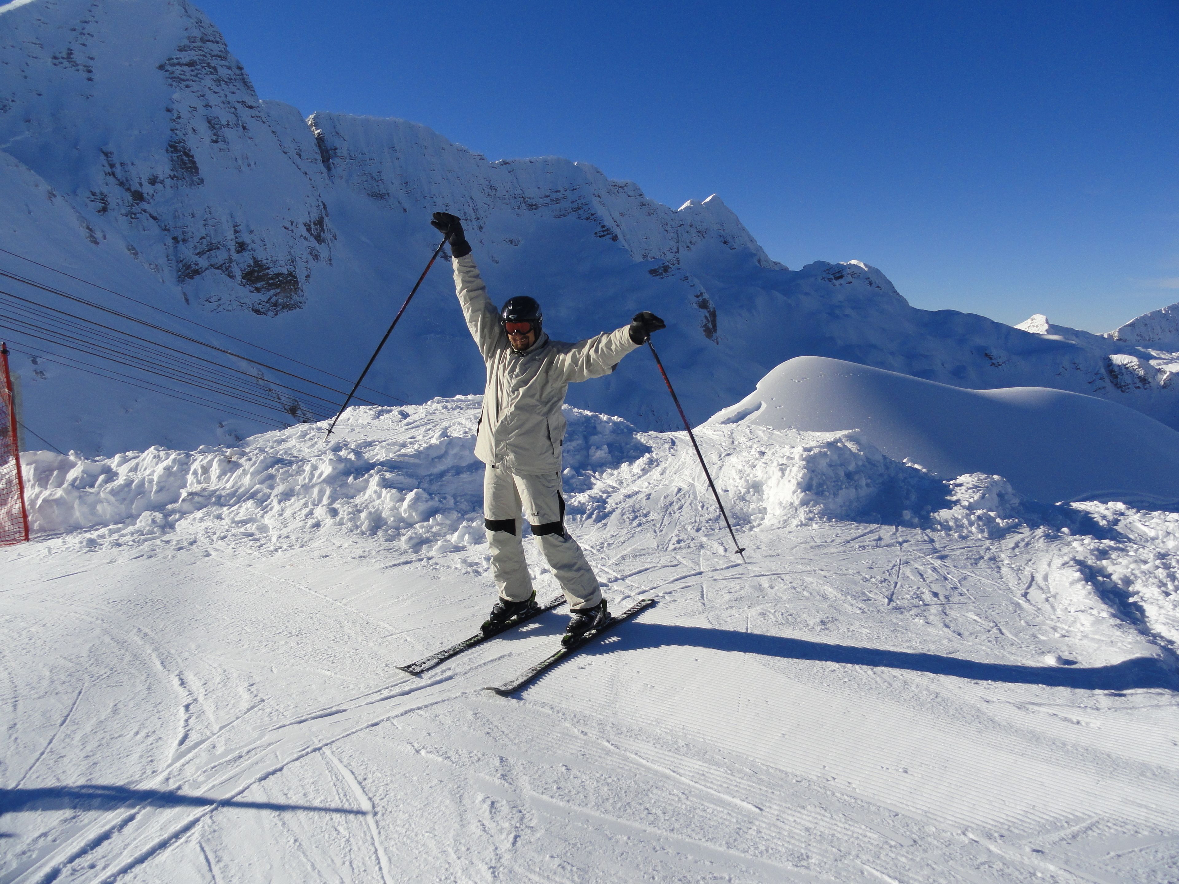 Eine Person fährt Ski auf einem verschneiten Hang, im Hintergrund sind Berge zu sehen.