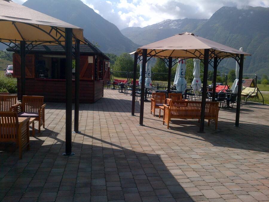 An outdoor patio with wooden furniture and a gazebo, set against a mountainous backdrop.