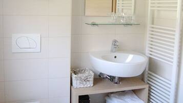 A bathroom with a toilet, sink, mirror, towel rack, and a shelf with toiletries.