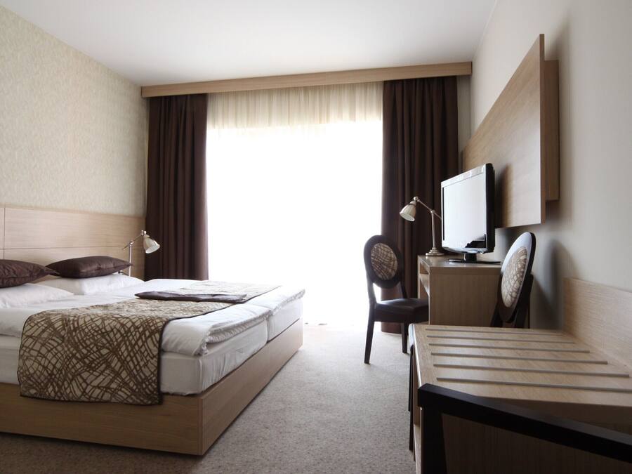A hotel room with a bed, a desk with a computer, a chair, and a television.