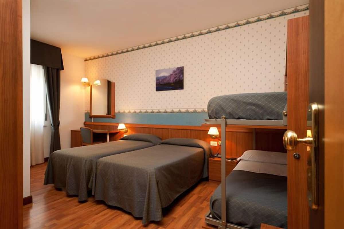 A room with two single beds, a bunk bed, a desk, and a chair.