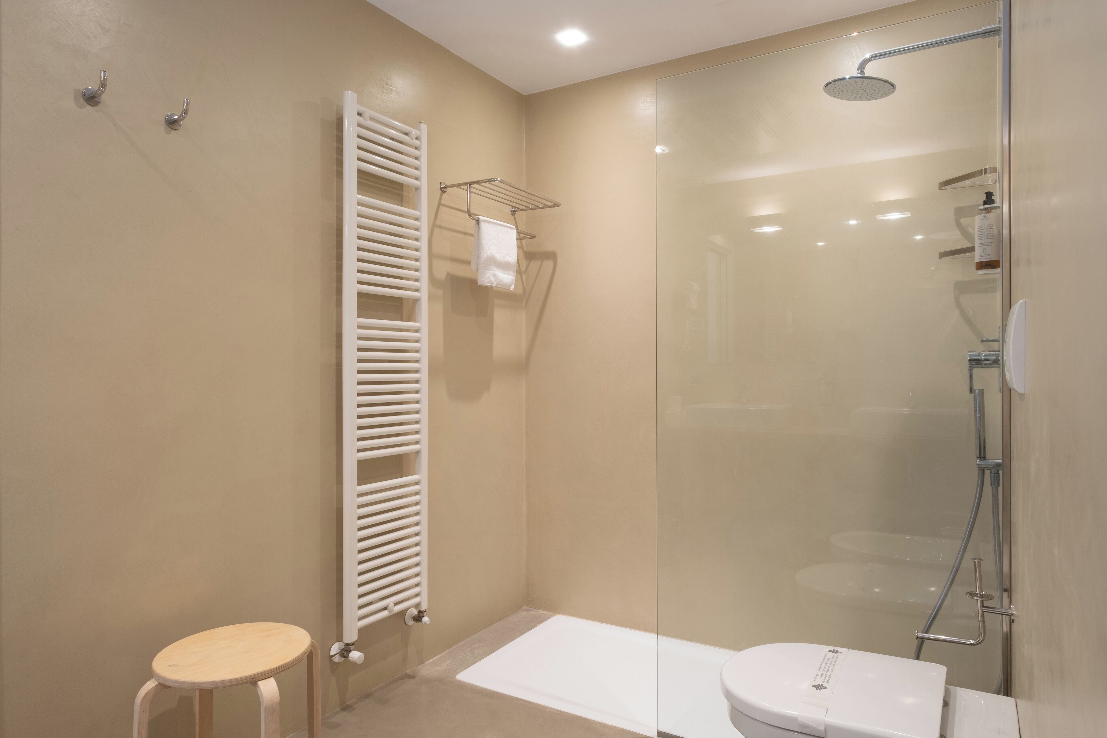 A modern bathroom with a glass-enclosed shower, a white bathtub, and a wooden stool.