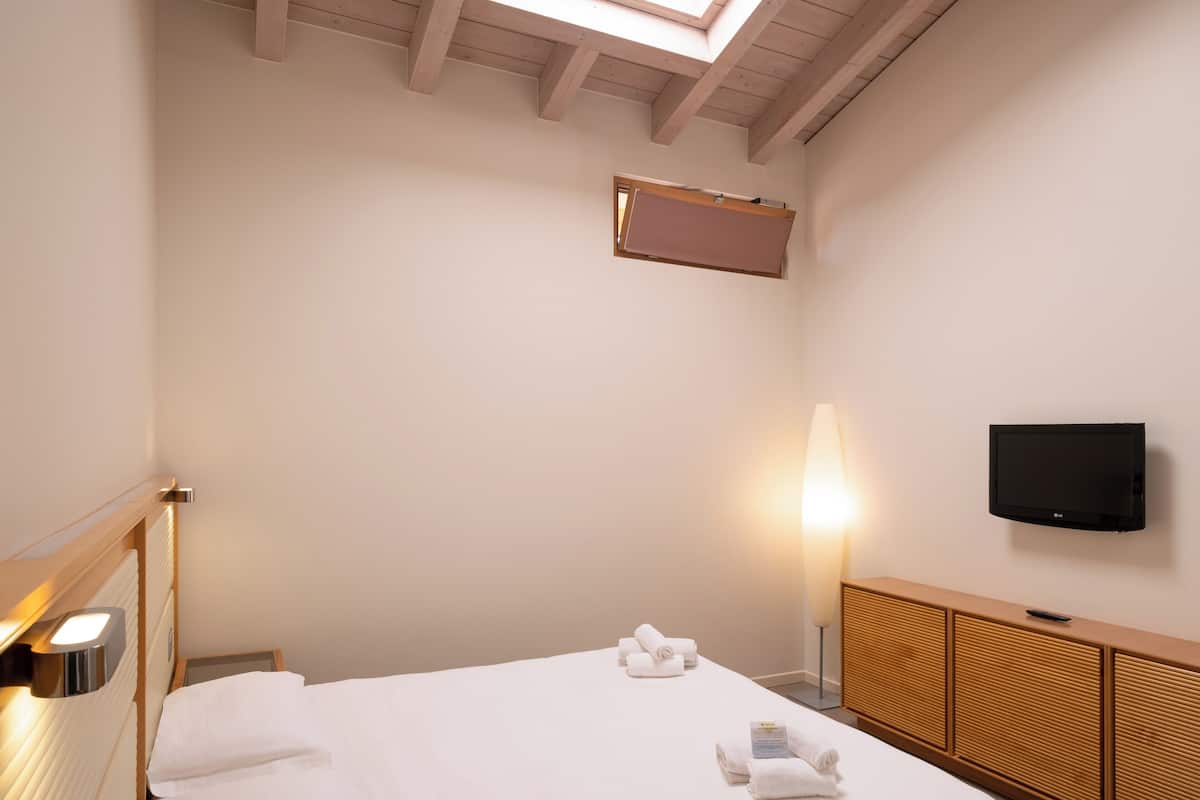Een hotelkamer met een bed, een aan de muur bevestigde televisie, een bedlamp en een houten kast.
