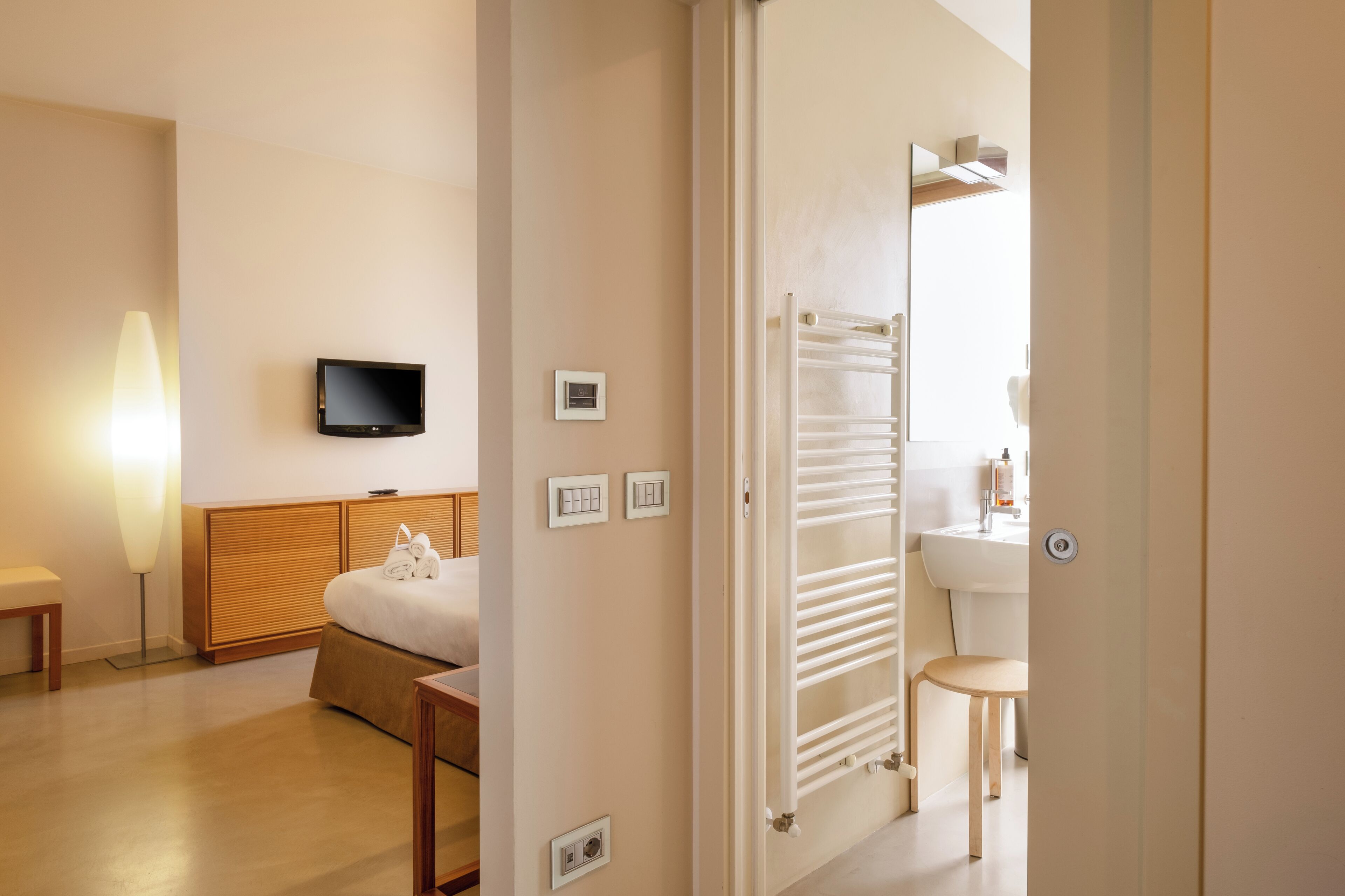 Une chambre d’hôtel comprenant un lit, une table de chevet, une lampe, une télévision et une salle de bain avec un lavabo et un miroir.