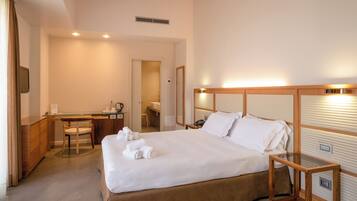 A hotel room with a large bed, a desk, a chair, a mirror, and a wooden headboard.