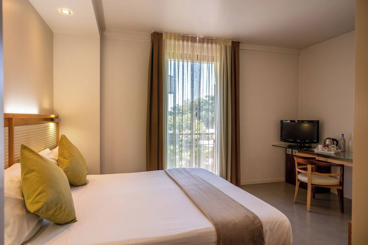 Een hotelkamer met een bed, een bureau met een televisie en een raam met gordijnen.