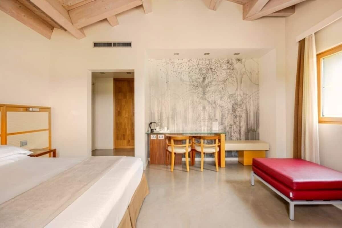 Een slaapkamer met een bed, een bureau met stoelen, en een rode bank.