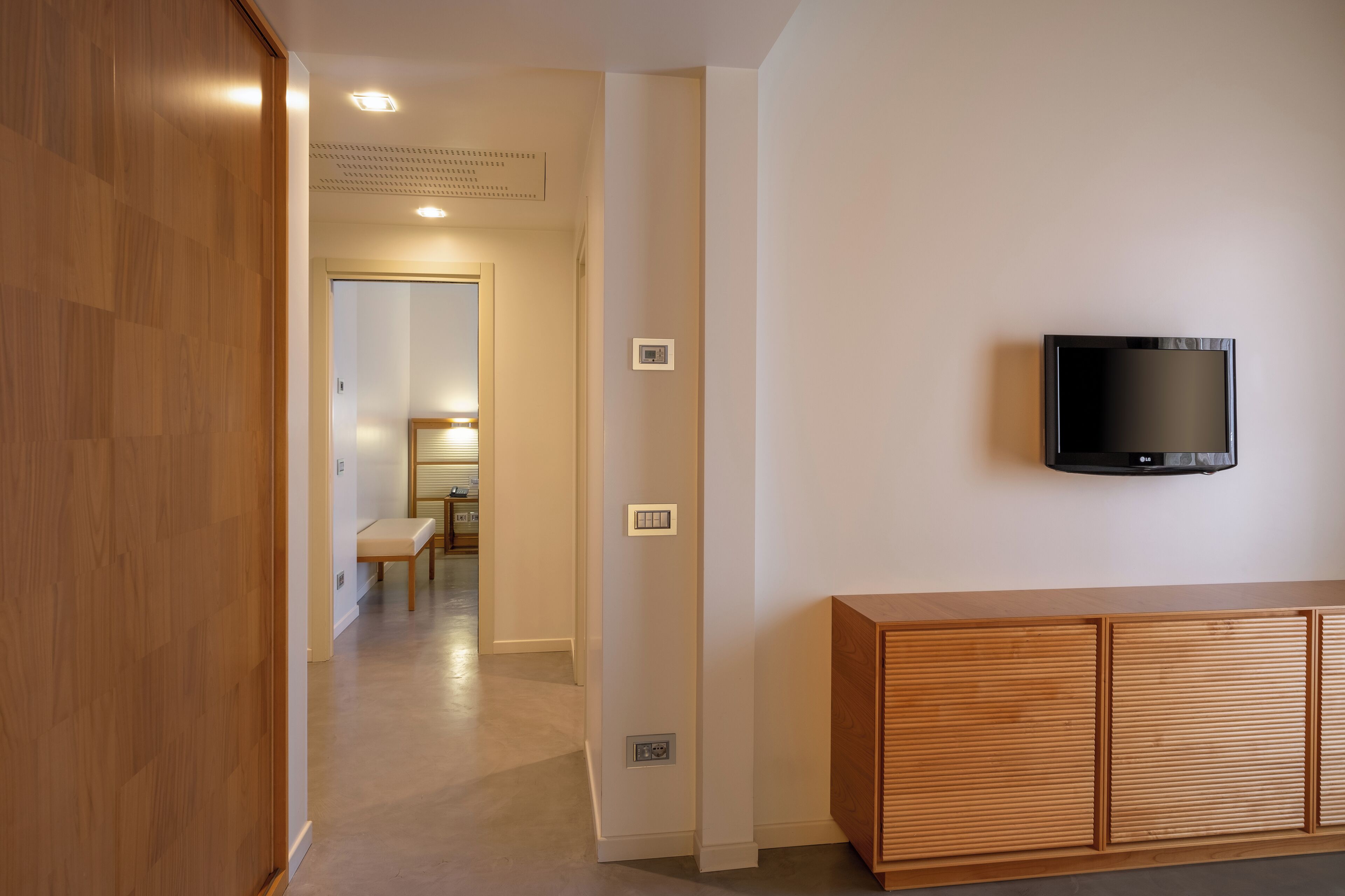 Ein modernes Interieur mit einem Holzkasten, einem flachbildfernseher an der Wand und einem Flur, der in einen anderen Raum führt.