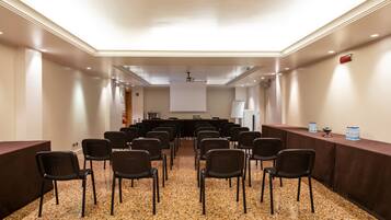 Een congreszaal met rijen stoelen, een scherm voor een presentatie en een presentatietafel.