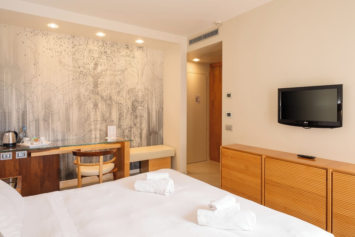 Een hotelkamer met een bed, een bureau met stoel, een televisie en een groot abstract kunstwerk aan de muur.