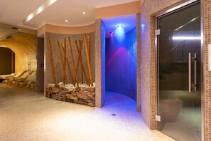 Un espace de détente avec un mur en pierre, des bambous et un élément décoratif aquatique illuminé de lumière bleue.