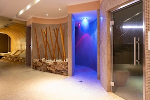 Zona de spa con pared de piedra, palos de bambú y una fuente de agua iluminada en azul.