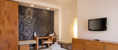 A hotel room with a large bed, a desk with a chair, a television mounted on the wall, and a wooden wardrobe.