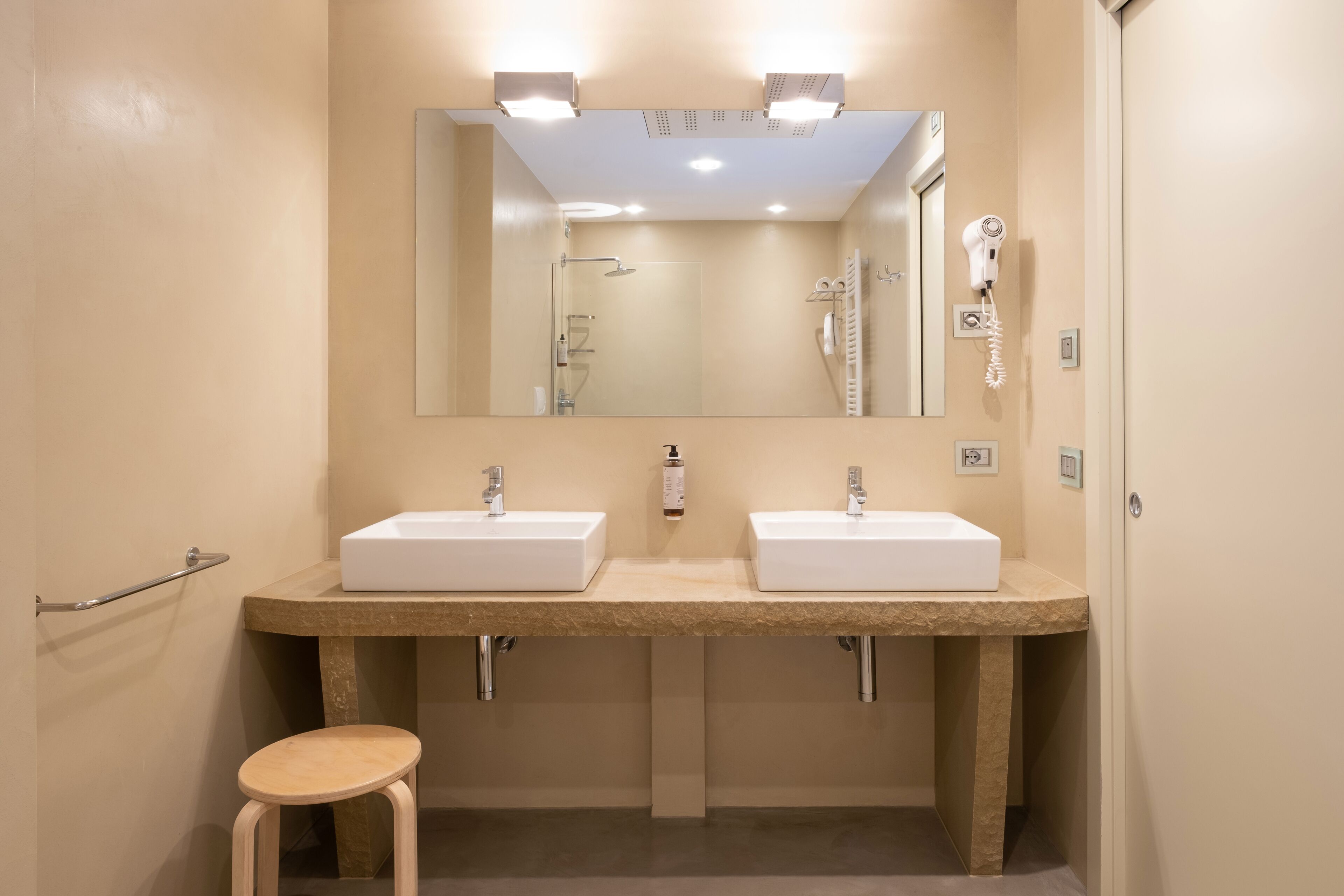 Un baño con dos lavamanos, un espejo y un secador de pelo en la pared.