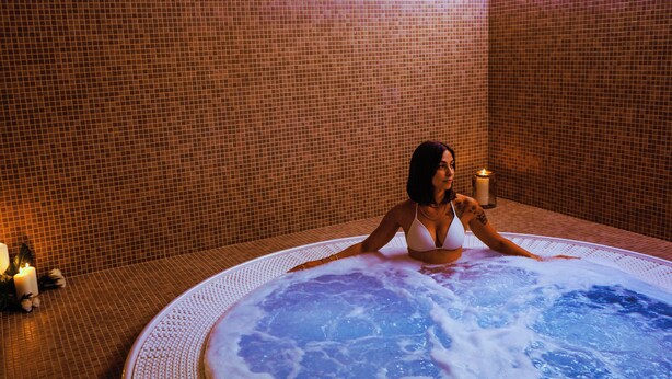 Une femme vêtue d’un bikini blanc est assise dans un jacuzzi, avec un mur carrelé en arrière-plan.