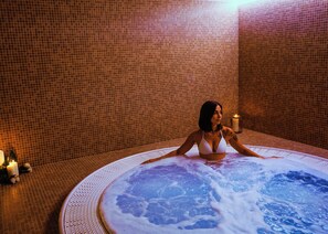 Une femme vêtue d’un bikini blanc est assise dans un jacuzzi, avec un mur carrelé en arrière-plan.