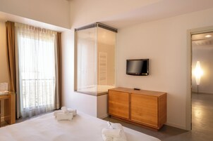 Habitación de hotel con una cama, un armario de madera, un televisor de pantalla plana y un ventanal con cortinas.