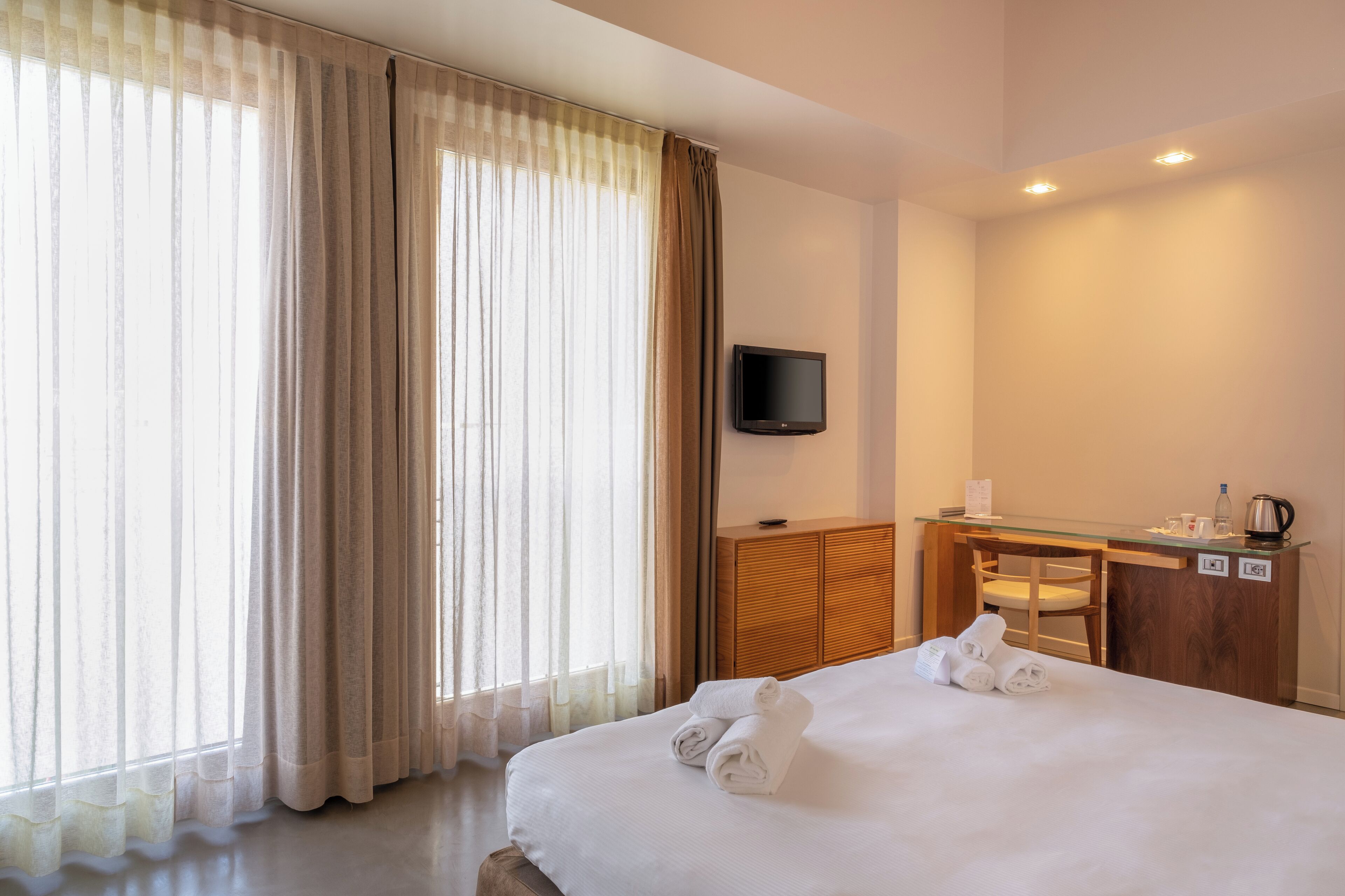 A hotel room with a bed, a desk, a chair, a television, and a window with curtains.