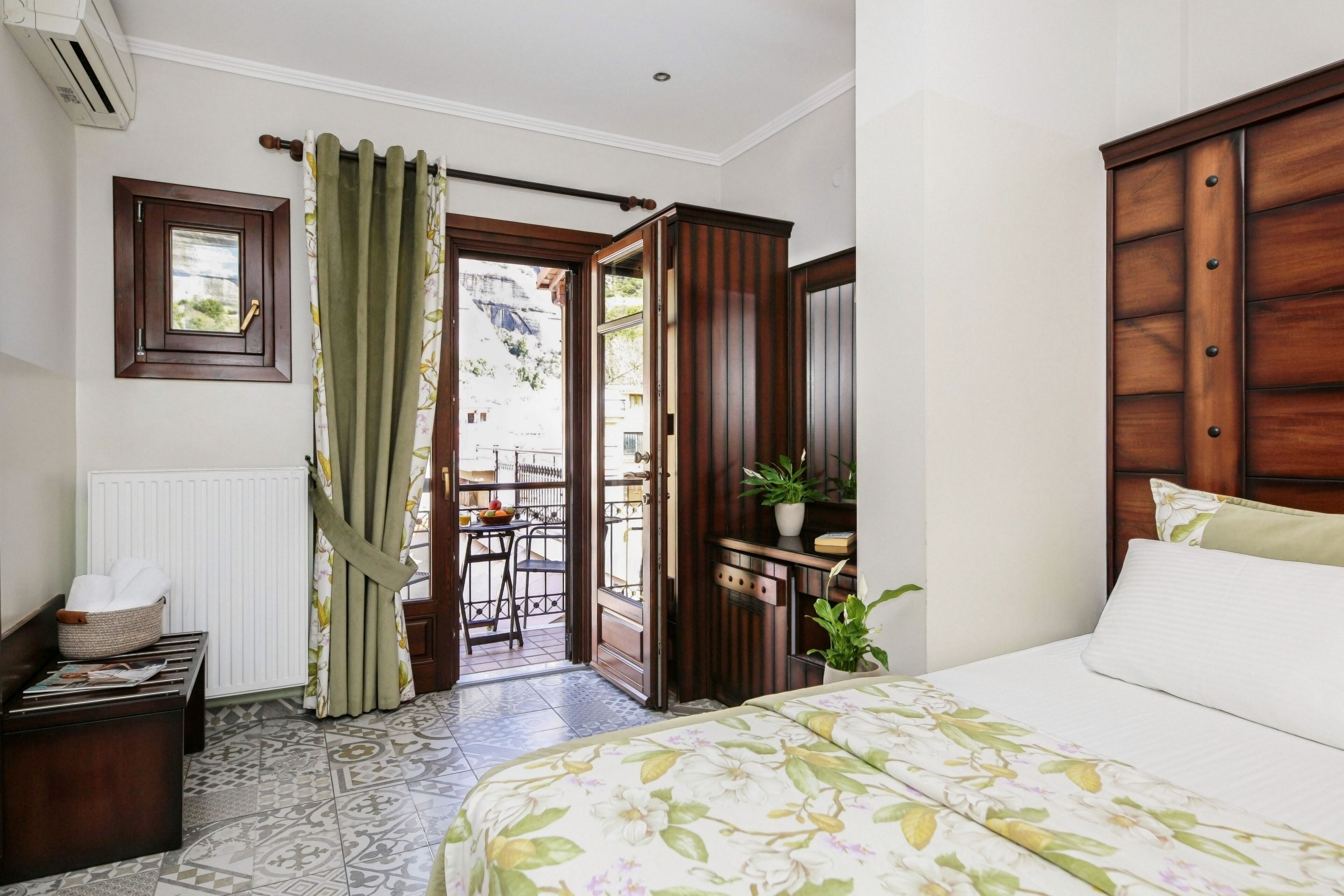 A bedroom with a bed, a wooden wardrobe, a radiator, a window, and a door leading to an outdoor area.