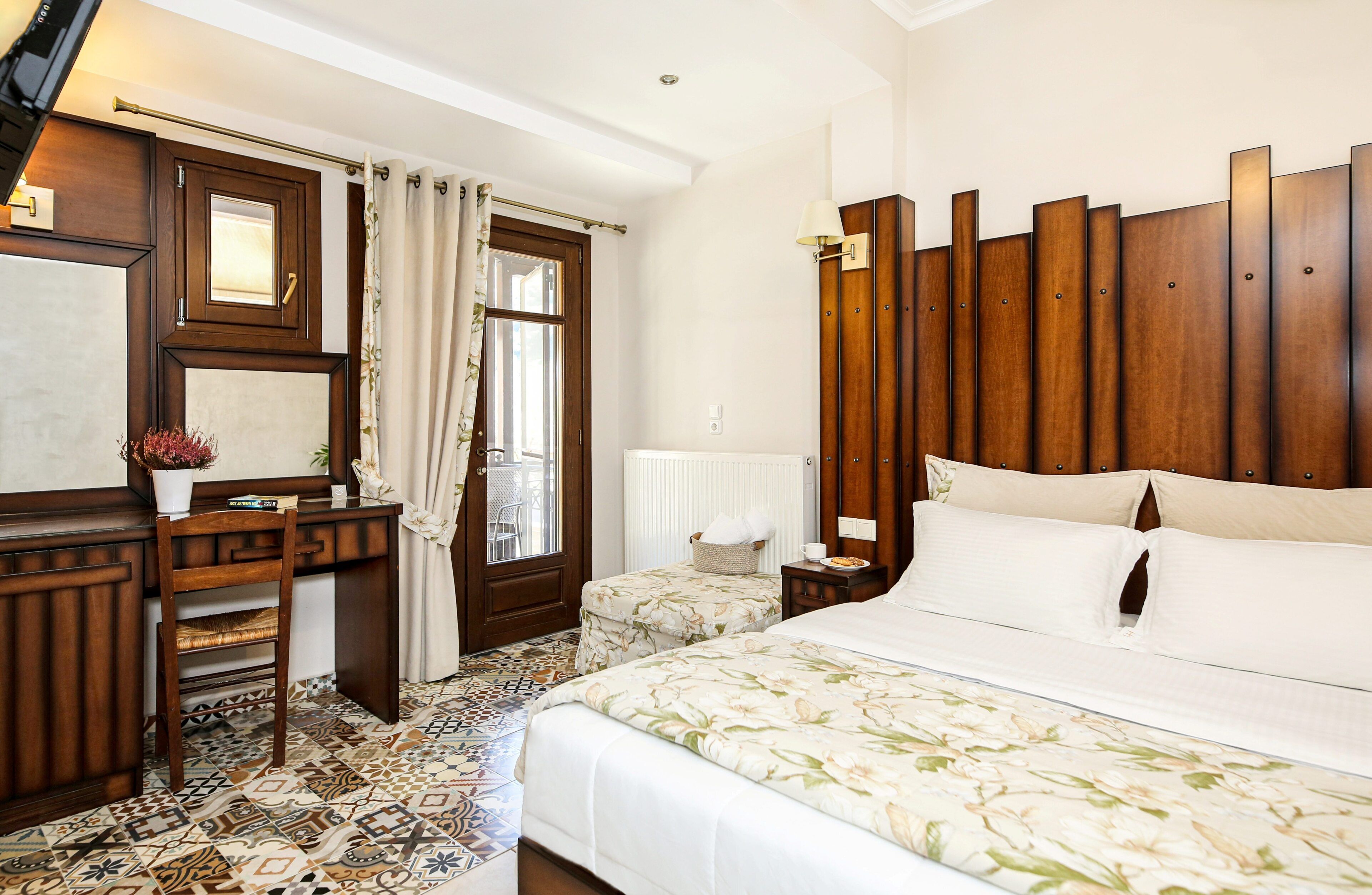 A bedroom with a bed, a desk, a chair, a window with curtains, a radiator, and a wooden headboard.