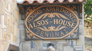 Un letrero que dice 'Habitaciones - Apartamentos' con el nombre 'Alos-House' y un jarrón decorativo debajo.