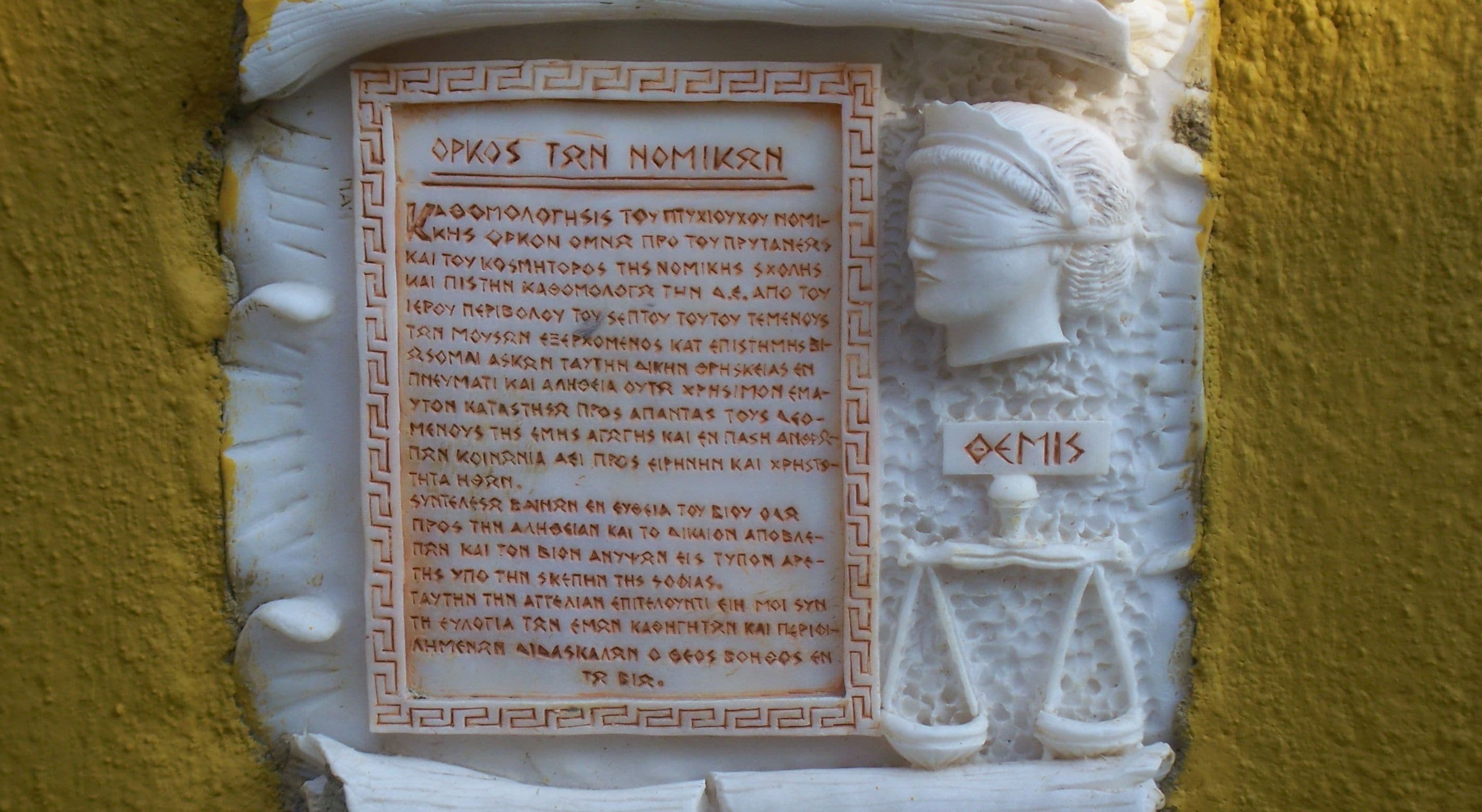 A carved stone plaque with ancient Greek text and a figure of a seated woman holding a scroll.