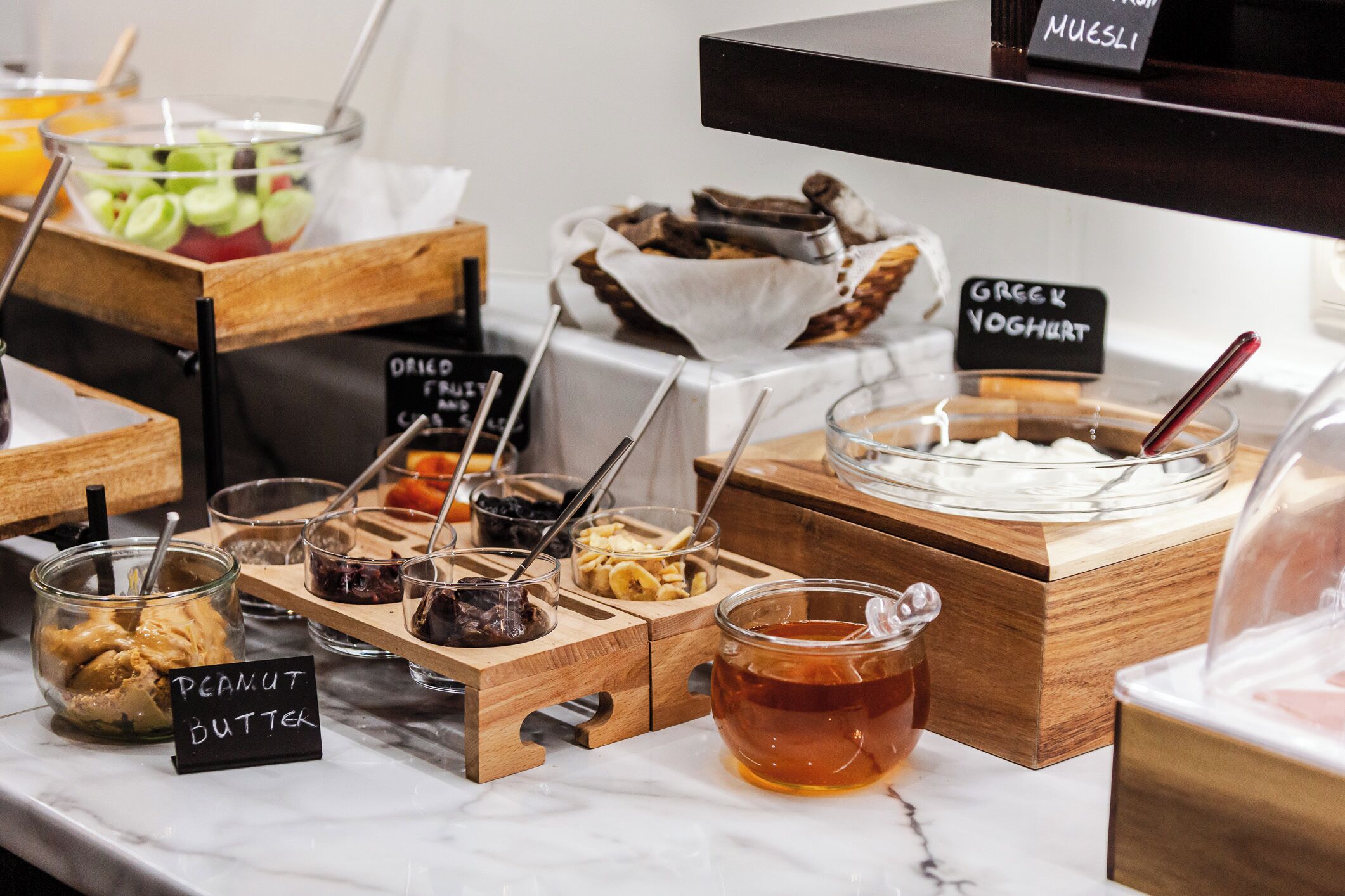 A food display with various items including a jar labeled 'peanut butter,' a bowl of 'Greek yogurt,' and a container of honey.