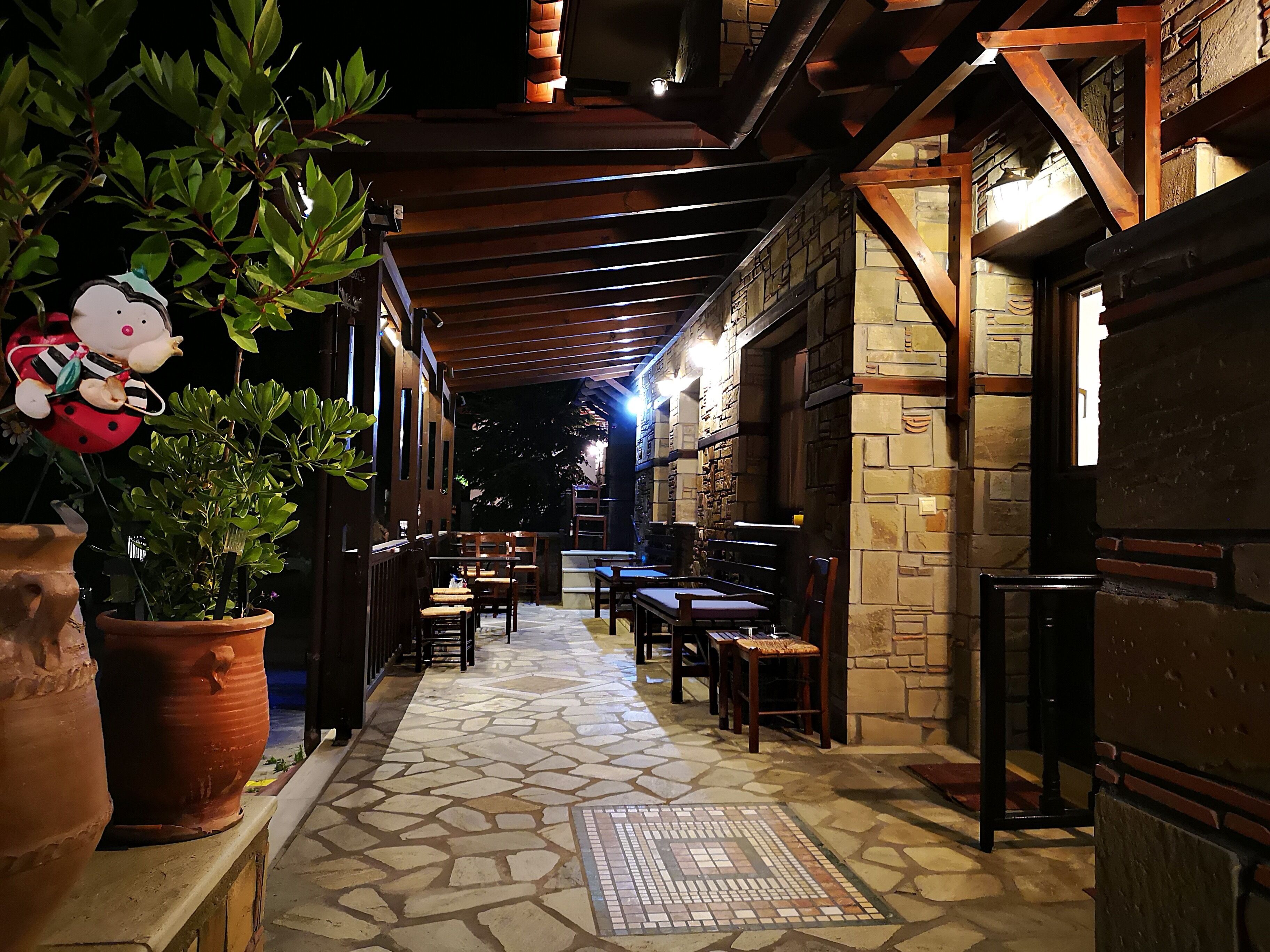 An outdoor patio area with stone flooring, wooden tables and chairs, and potted plants.