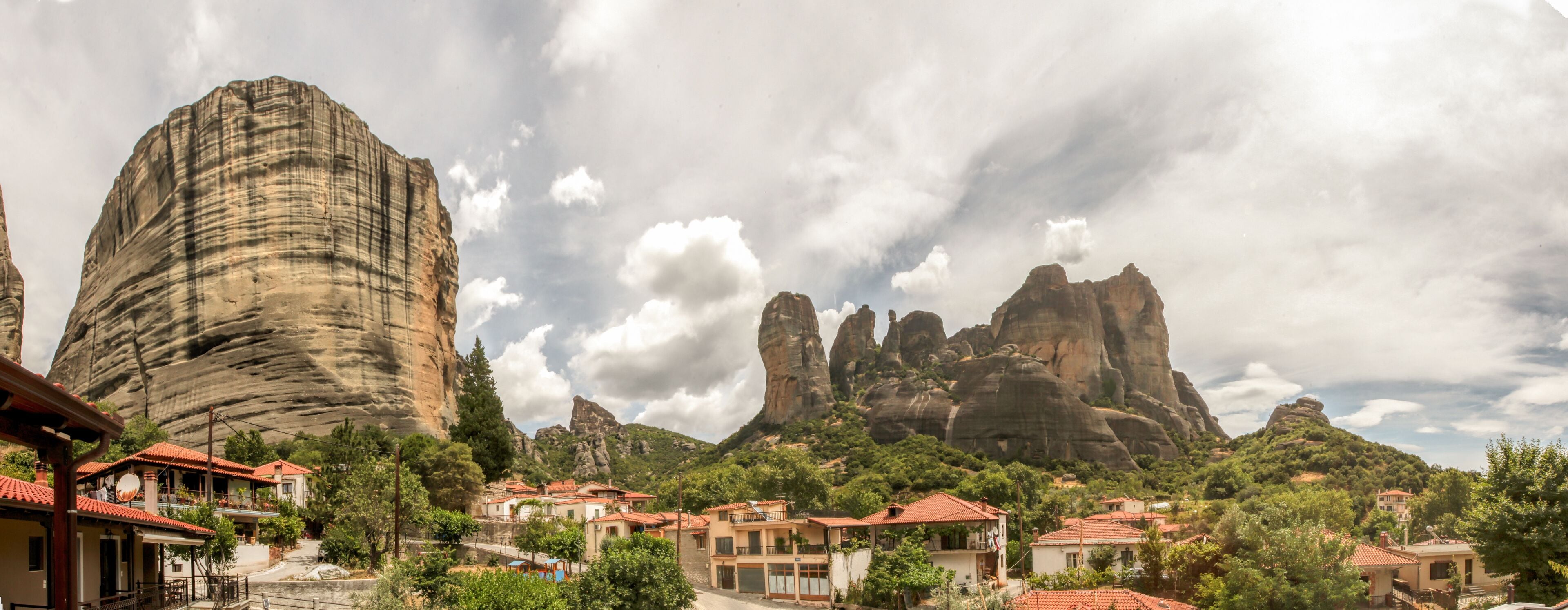 A village with red-roofed buildings, a prominent rock formation, and lush greenery.