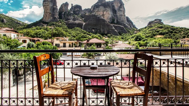Un balcón con dos sillas de madera y una mesa, con vistas a un paisaje montañoso con formaciones rocosas.