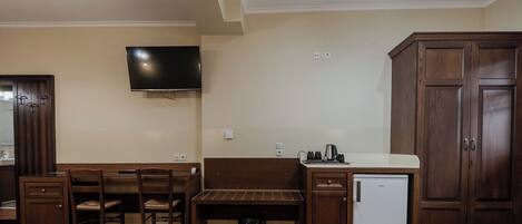 A kitchen with a dining table, chairs, a bench, a refrigerator, and a TV mounted on the wall.