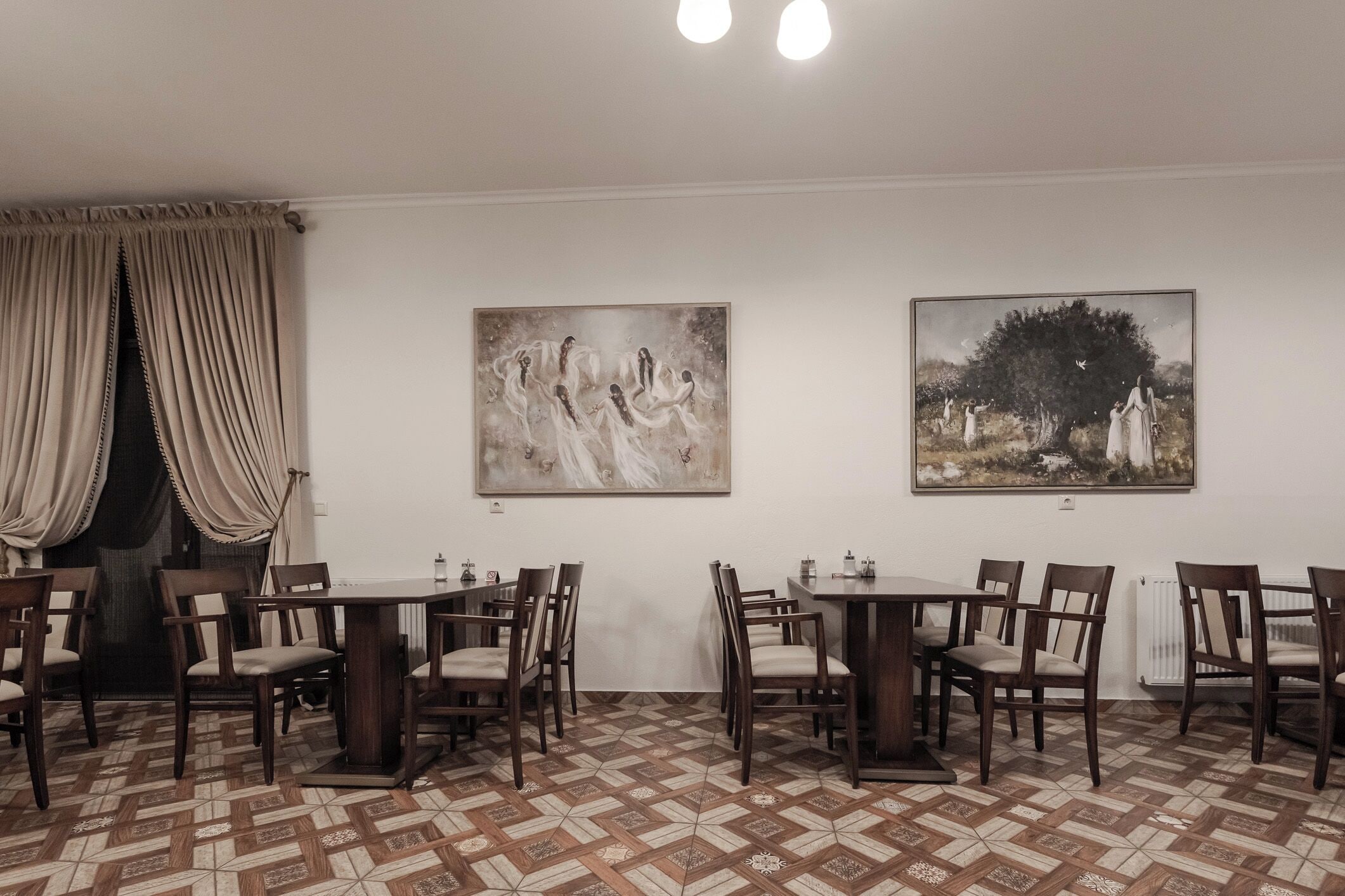 A dining area with two tables and chairs, a patterned floor, and two paintings on the wall.
