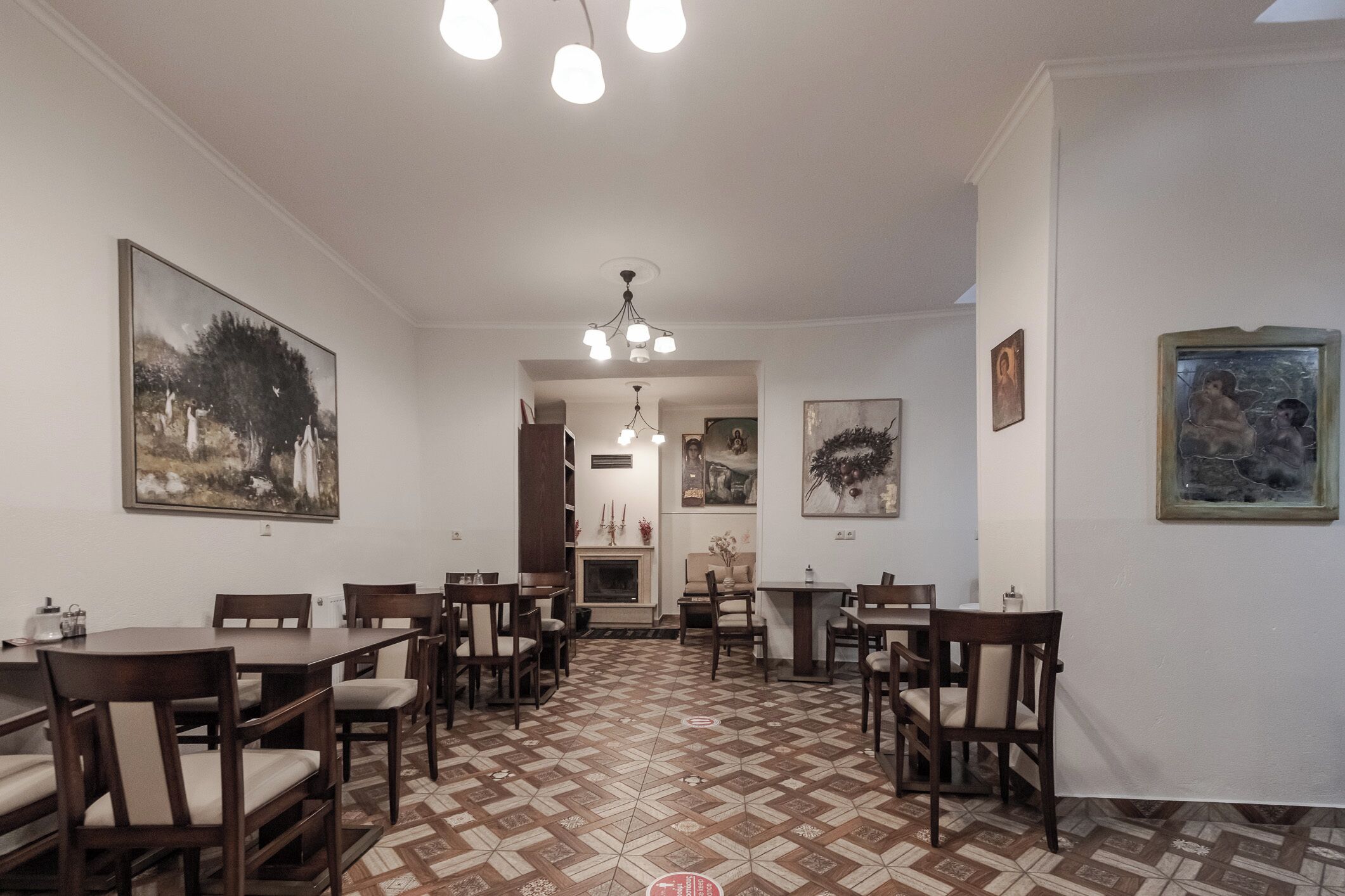 A dining area with multiple tables and chairs, a patterned floor, and artwork on the walls.