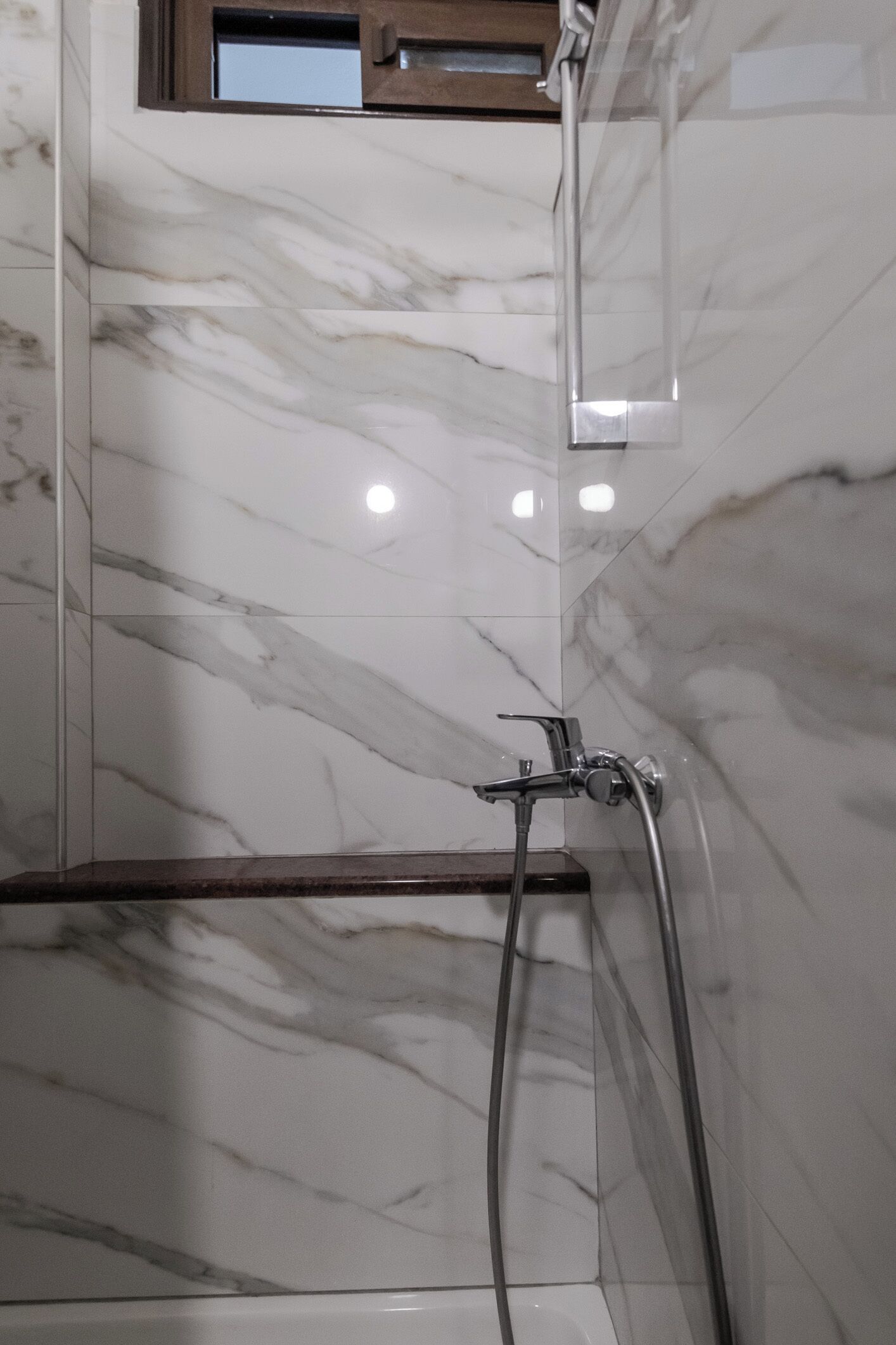 Un baño con paredes de mármol, una ducha y un estante de madera.