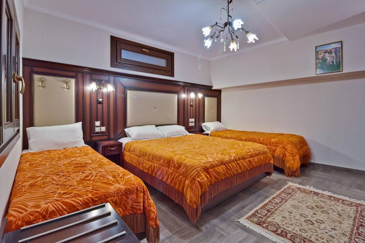 A hotel room with two beds, a wooden headboard, a chandelier, and a patterned rug.
