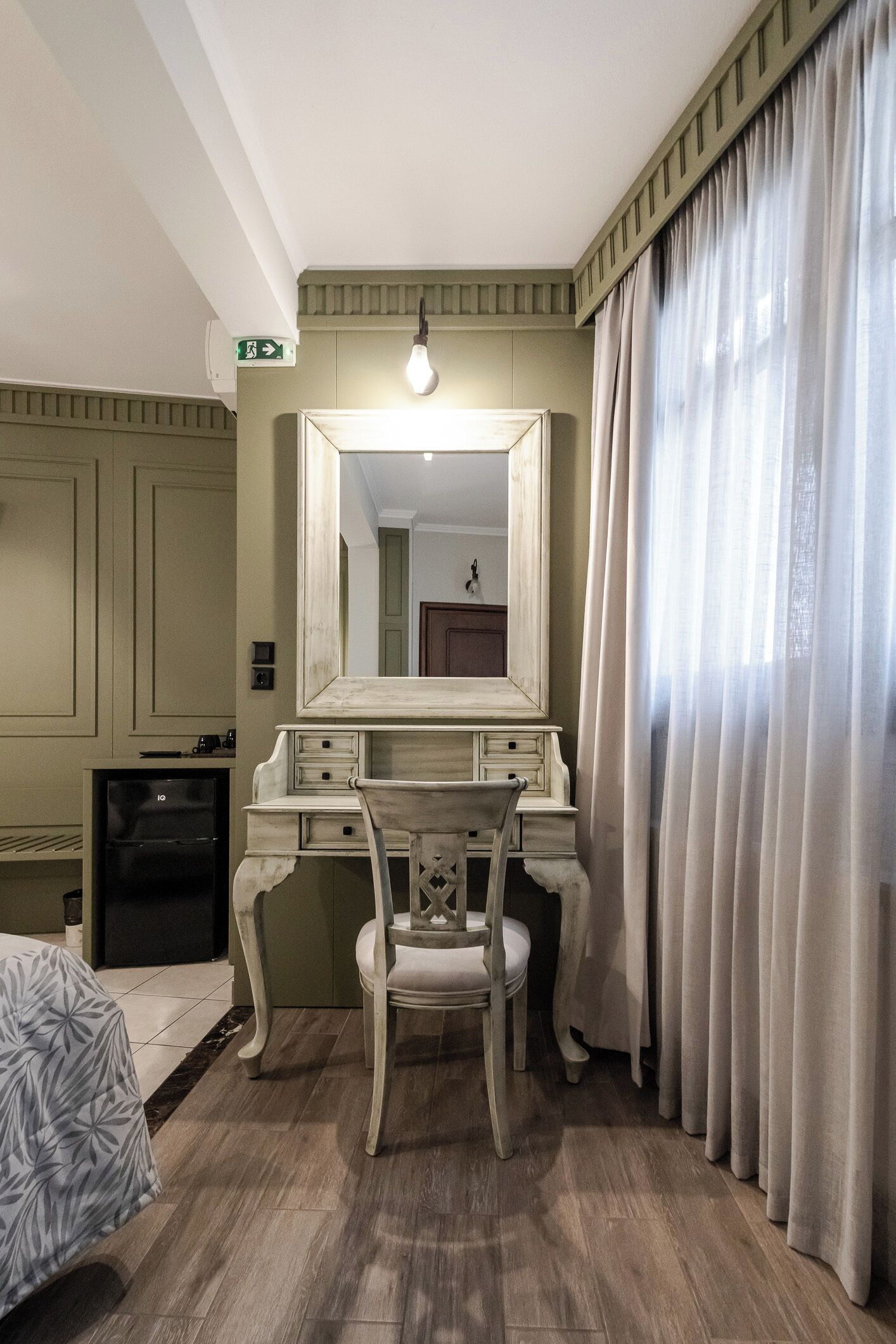 Una habitación con tocador, una silla, una cama, un escritorio y un espejo.