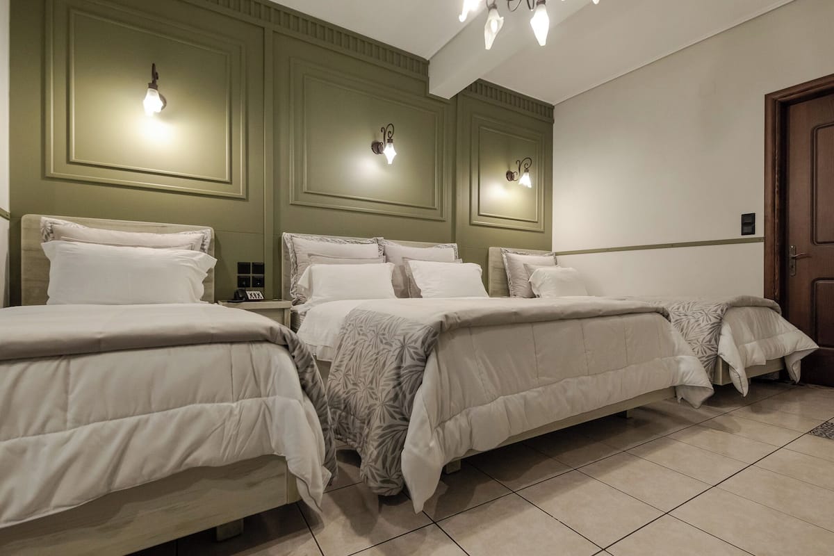 A hotel room with three beds, a wooden door, and wall-mounted light fixtures.