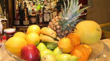 Uma tigela de frutas com diversas frutas e um bar com garrafas de bebidas ao fundo.