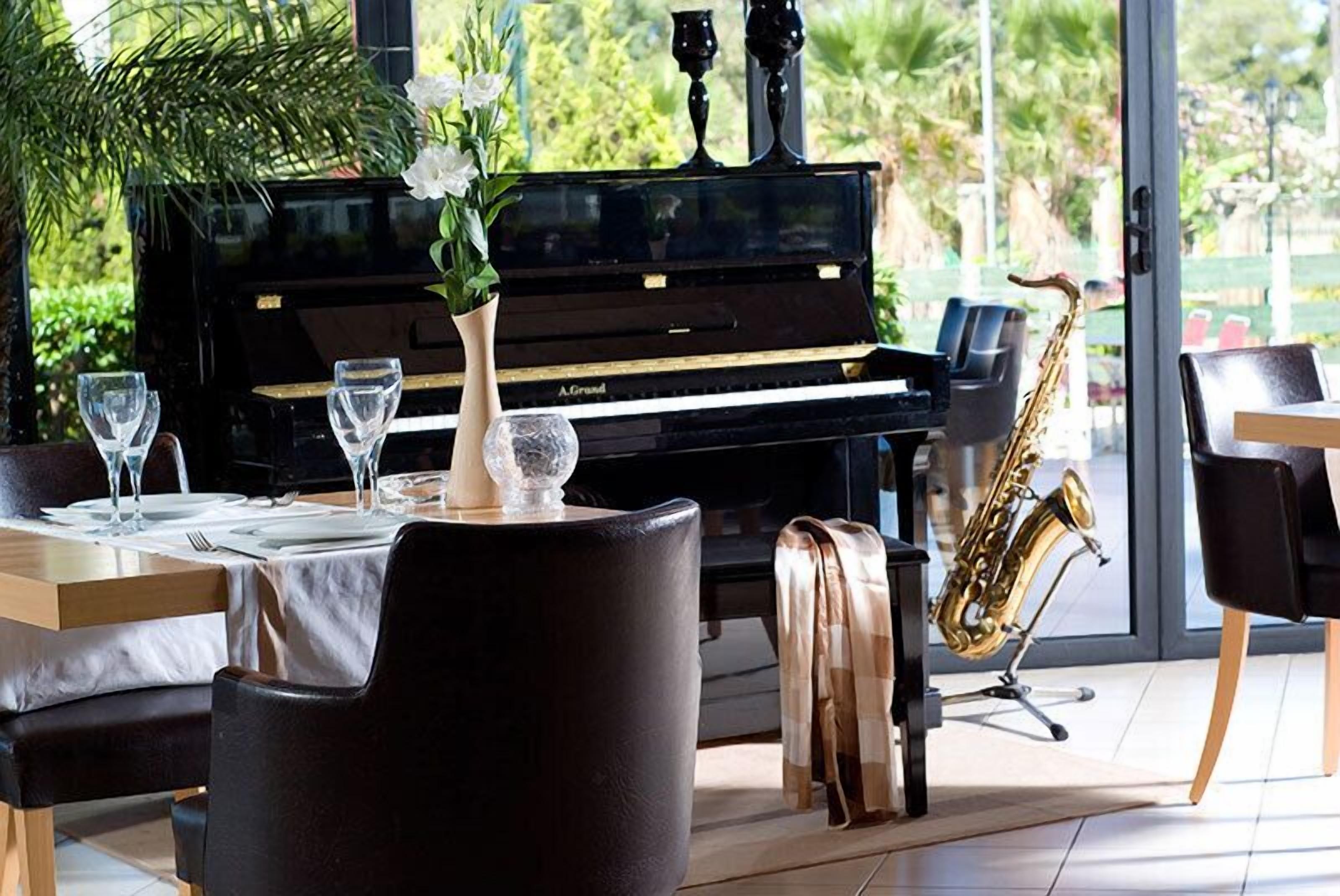Uma sala de jantar com piano e saxofone, um vaso de flores e uma mesa posta para dois.