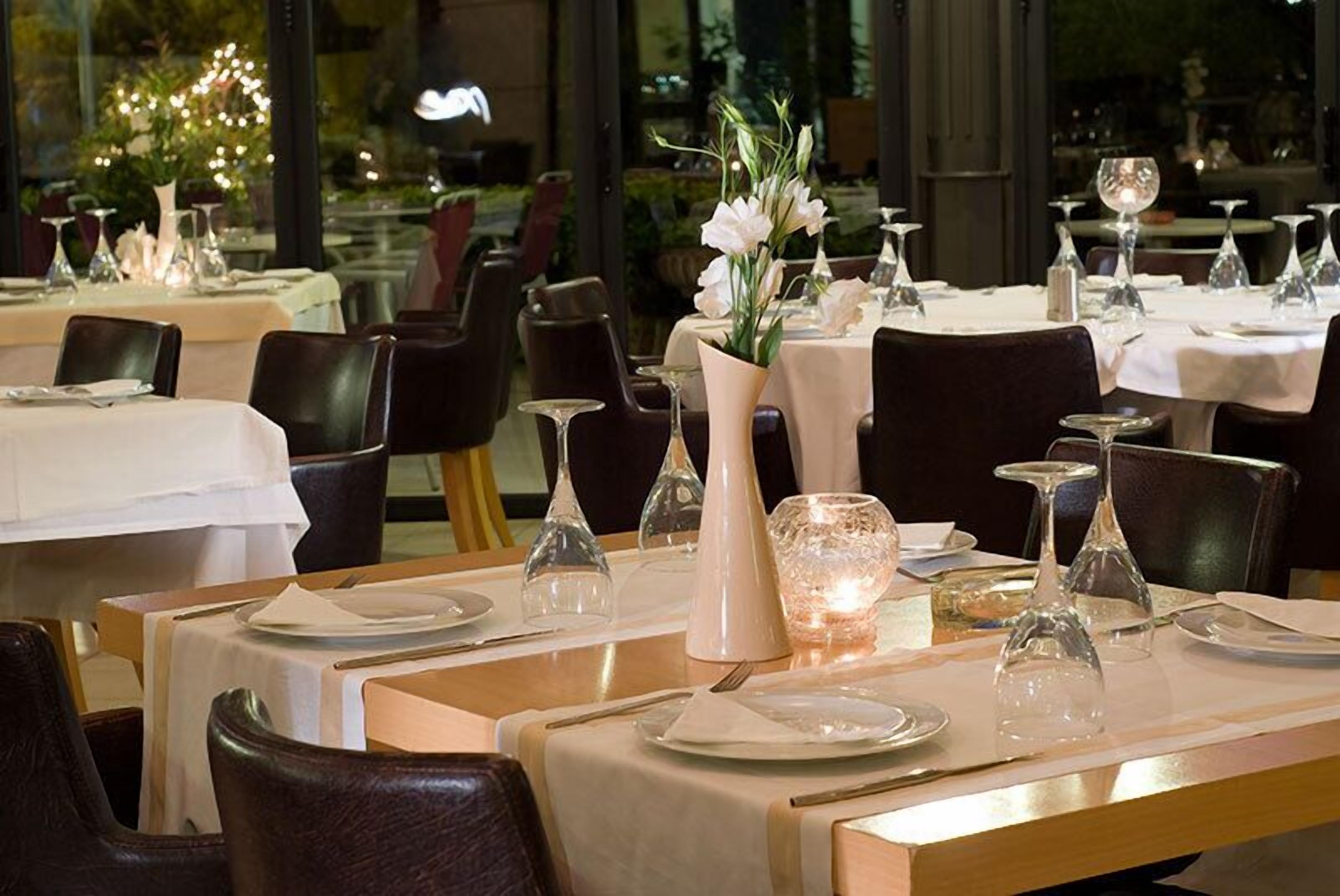 A restaurant with tables set for dining, featuring white tablecloths, elegant glassware, and floral centerpieces.