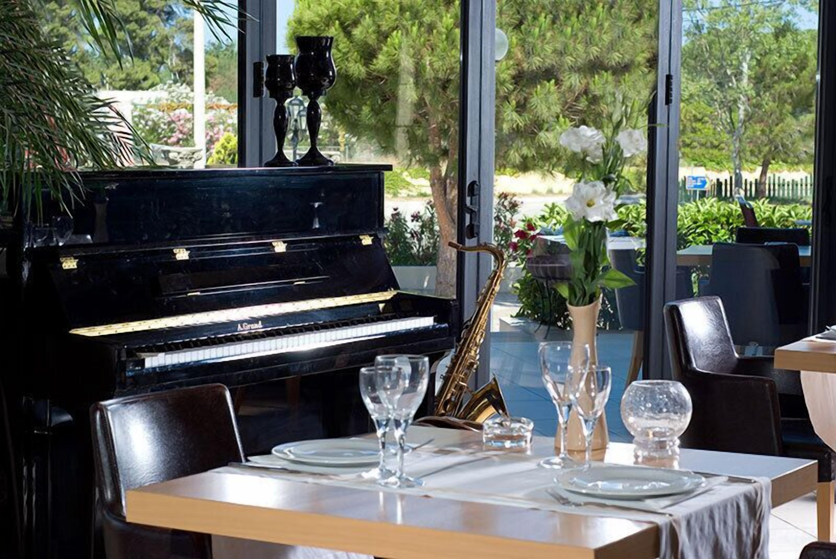 A dining area with a piano, dining table set with plates, glasses, and a vase with flowers.