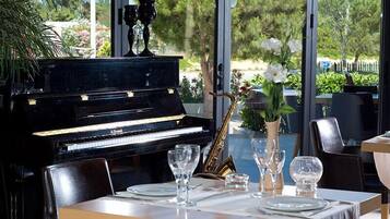 A dining area with a piano, dining table set with plates, glasses, and a vase with flowers.