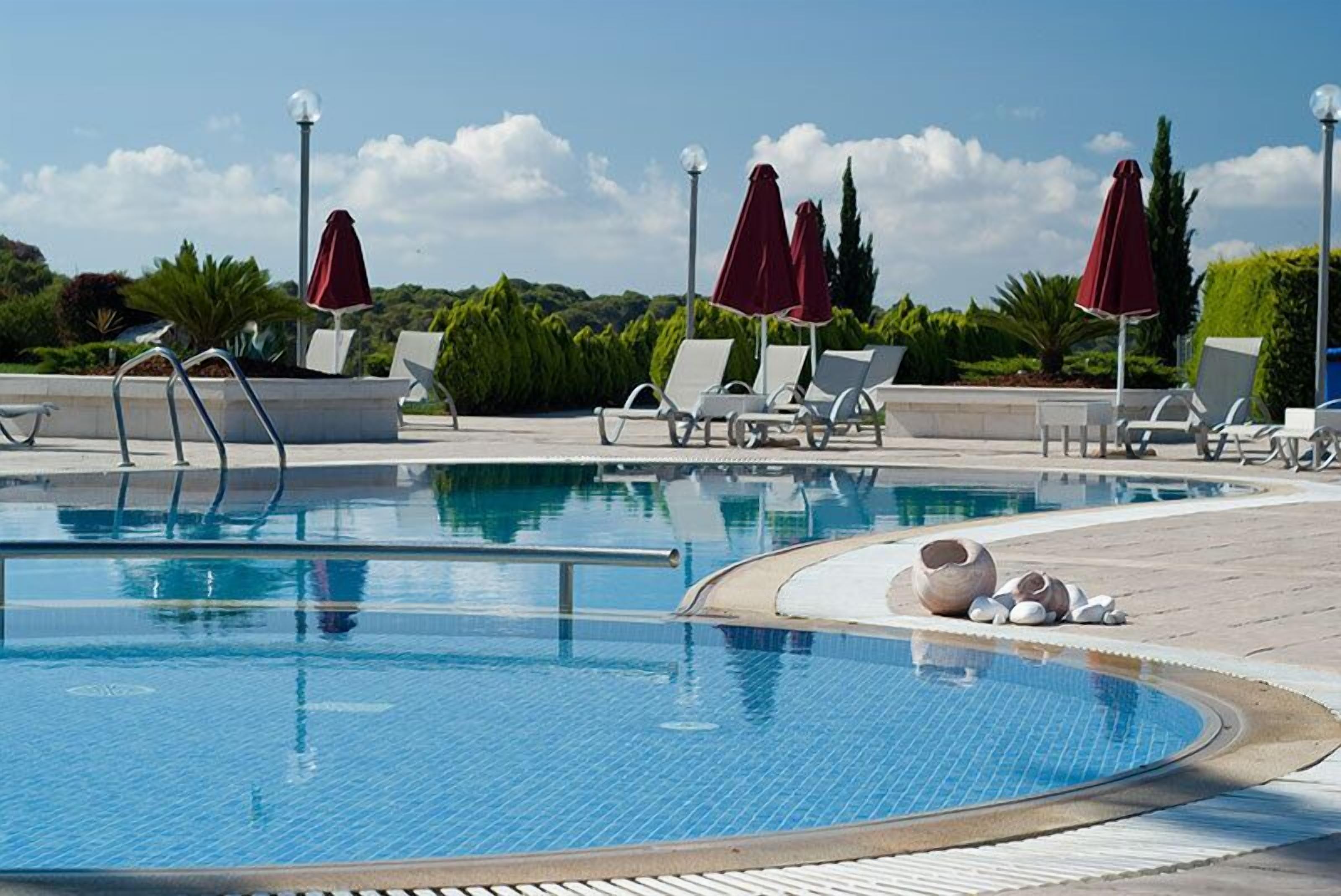 Ein Pool mit Liegestühlen und Sonnenschirmen, umgeben von viel Grün.